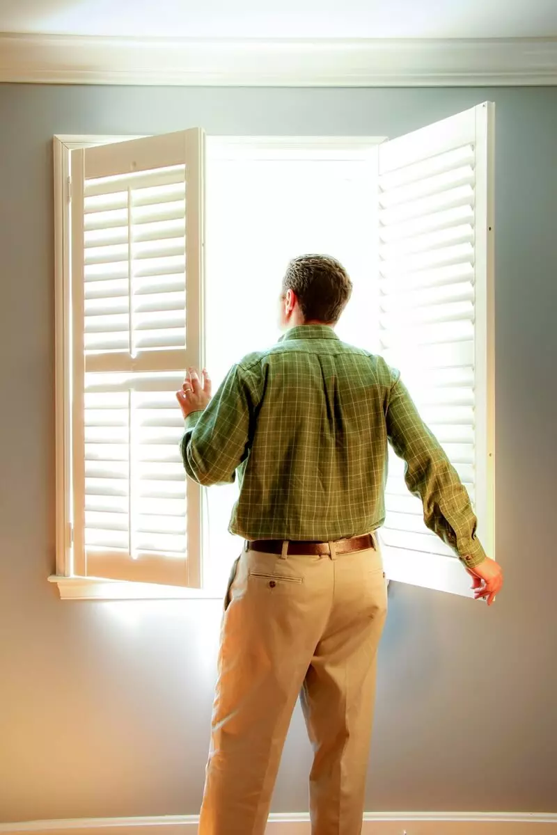 Uomo con pantaloni gialli e camicia verde che guarda fuori da una finestra